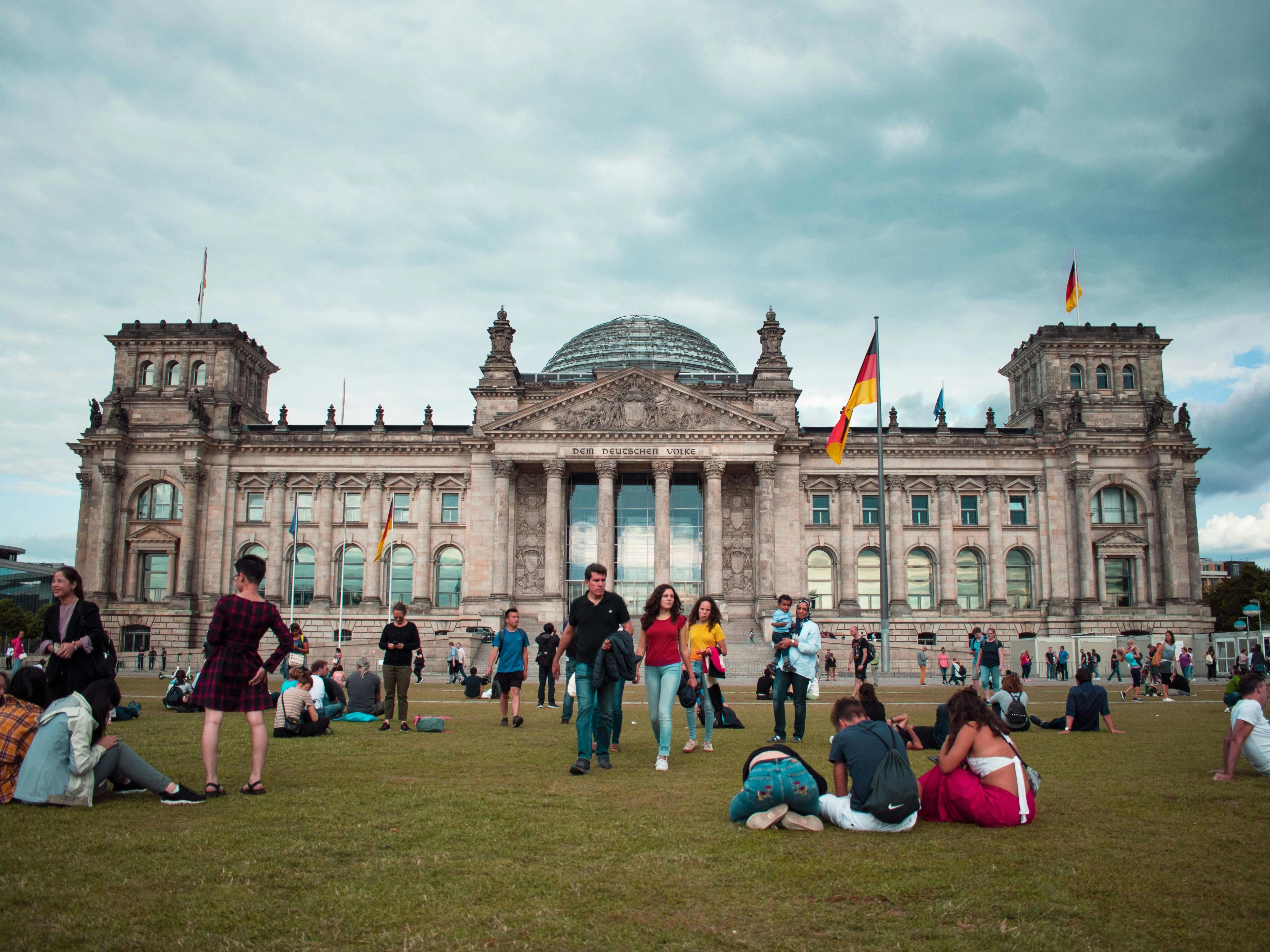 Auf der Wiese vor dem Bundestag in Berlin sitzen einige junge und ältere Menschen. 